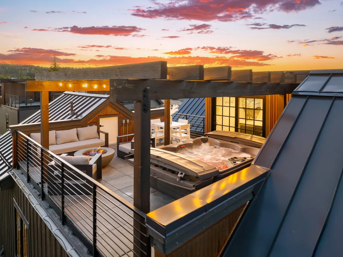A rooftop terrace with a steamy hot tub, inviting outdoor seating, string lights illuminating the space, and a striking sunset sky overhead. The scene is set for relaxation and evening gatherings under the stars, evoking both serenity and sociability.
