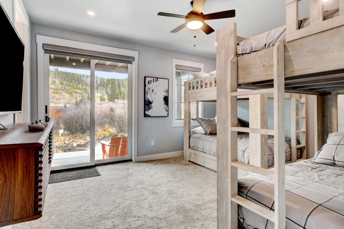 A playful bunk room with a large window, bunk bed, television, and wall art. The space is designed for fun and relaxation, perfect for children or friends, with plenty of natural light and cozy bedding.
