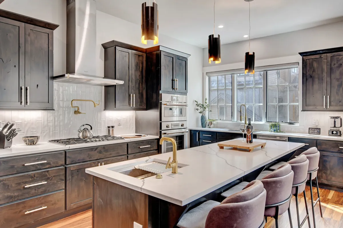 A gourmet kitchen with a prominent island, sleek modern cabinetry, stylish pendant lighting, and a window streaming in natural daylight. The ample counter space and quality appliances invite culinary creativity and social interaction.