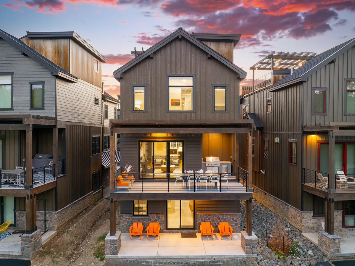 A striking view of the villa’s exterior, highlighting modern architectural lines, vibrant orange chairs on the balcony, expansive windows, and a scenic backdrop. The setup suggests spaces for both private relaxation and lively outdoor gatherings.