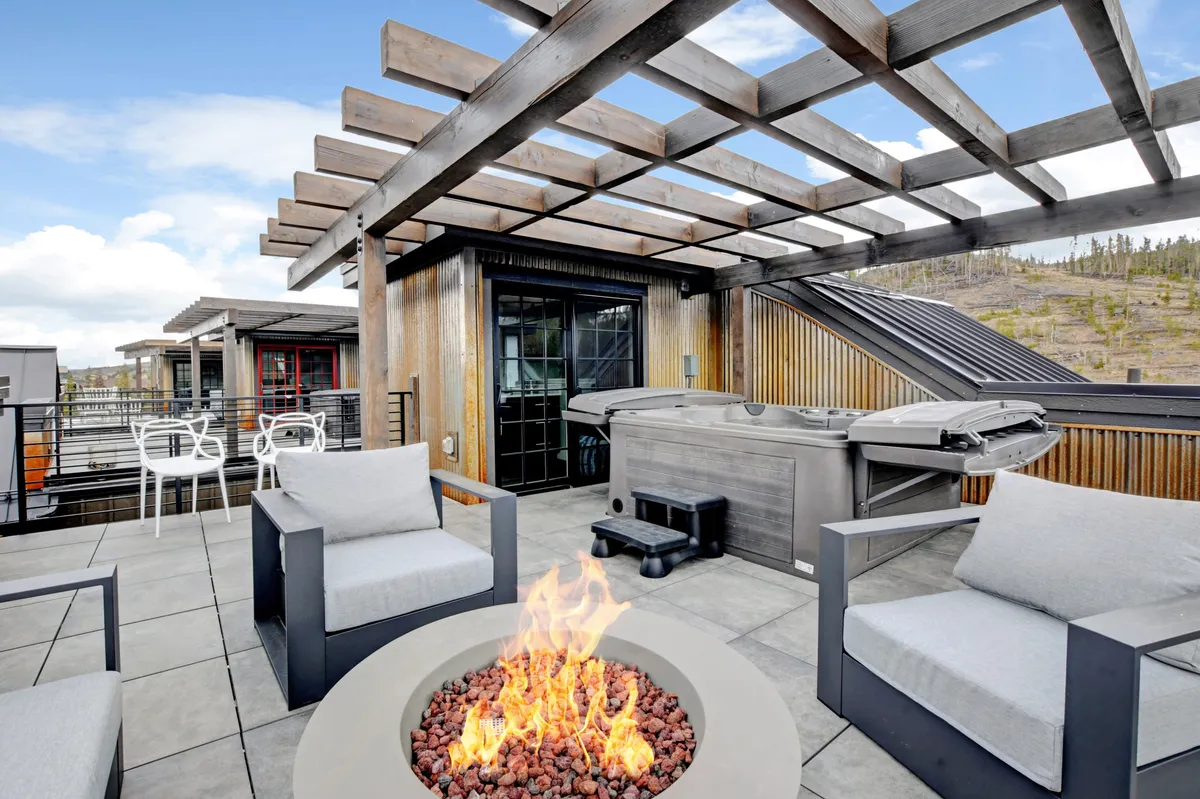 An inviting outdoor space featuring a fire pit, hot tub, pergola, and ample seating, all set within scenic surroundings. The atmosphere is cozy and social, hinting at shared evenings under the stars and a space for relaxation after a day of adventure.
