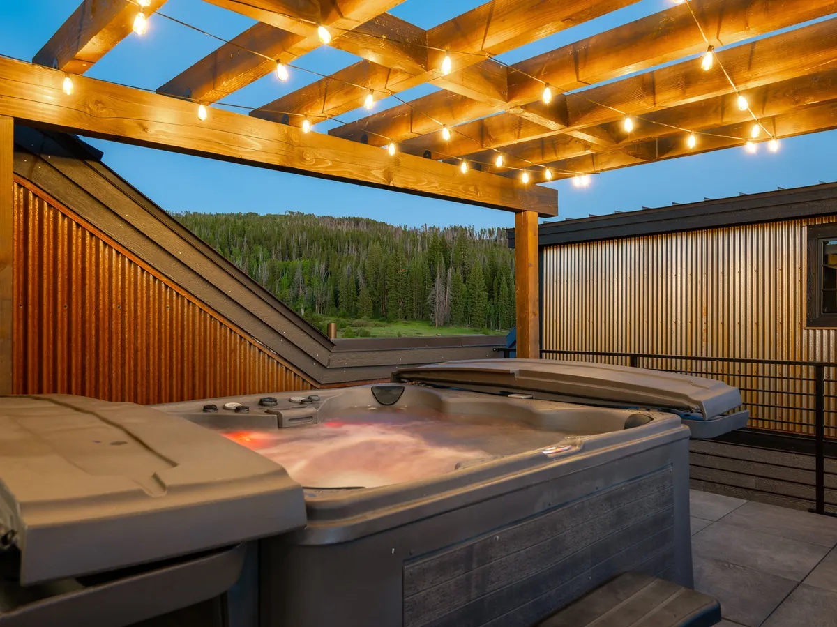 An inviting rooftop hot tub under a wooden pergola, accented by string lights, with sweeping mountain views in the background. The tranquil scene suggests both relaxation and connection to nature, perfect for unwinding after work.