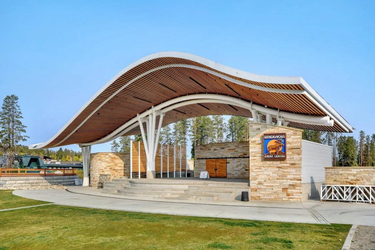 This image showcases the curved roof structure and stone walls of the outdoor Rendezvous Event Center at Hideaway Park. The open stage area is set for community gatherings, live performances, and local celebrations.