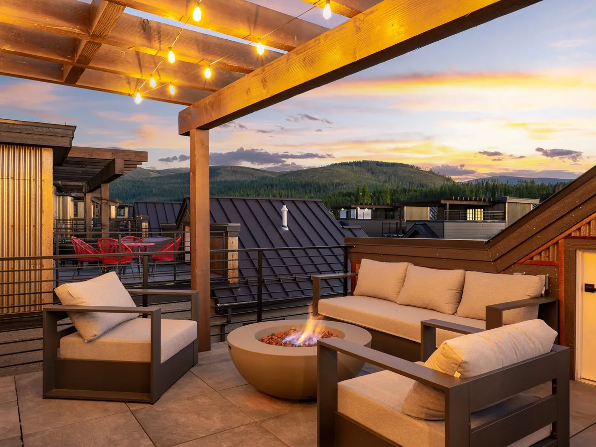 A cozy outdoor seating area encircling a fire pit, framed by string lights and a panoramic view of the Rockies. The scene evokes social gathering potential, relaxation, and a deep connection with the surrounding environment.