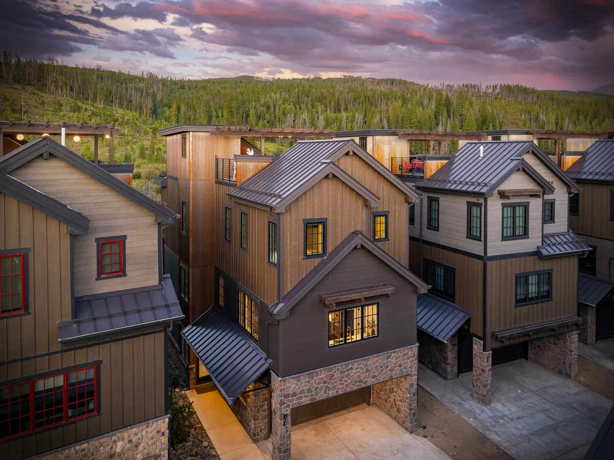 This exterior image showcases the villa's modern architecture set against natural surroundings and a stunning sunset sky. The view hints at the home's connection to the outdoors and its proximity to recreational spaces, with visible balconies and gathering areas that suggest relaxation and adventure.