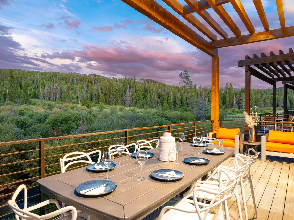 A beautiful outdoor dining area with a table under a pergola, surrounded by comfy seating and panoramic mountain views. The scene suggests both lively gatherings and peaceful evenings, seamlessly blending relaxation with outdoor entertainment.