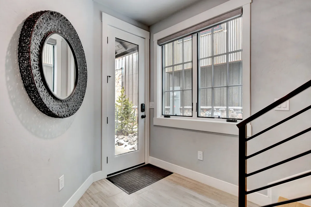 A bright and welcoming entrance foyer, featuring a round mirror, large window with views outside, and a staircase leading further into the home. The ambiance is inviting and open, giving a sense of arrival and transition.