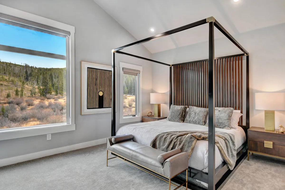 A serene bedroom featuring a four-poster bed, large window with views of nature, abstract wall art, and nightstands with lamps. The room is filled with natural light and exudes calm, inviting rest and relaxation.